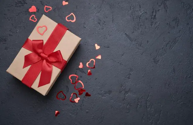 Valentine's day greeting card. Gift box with red ribbon and heart figurines on black background Top