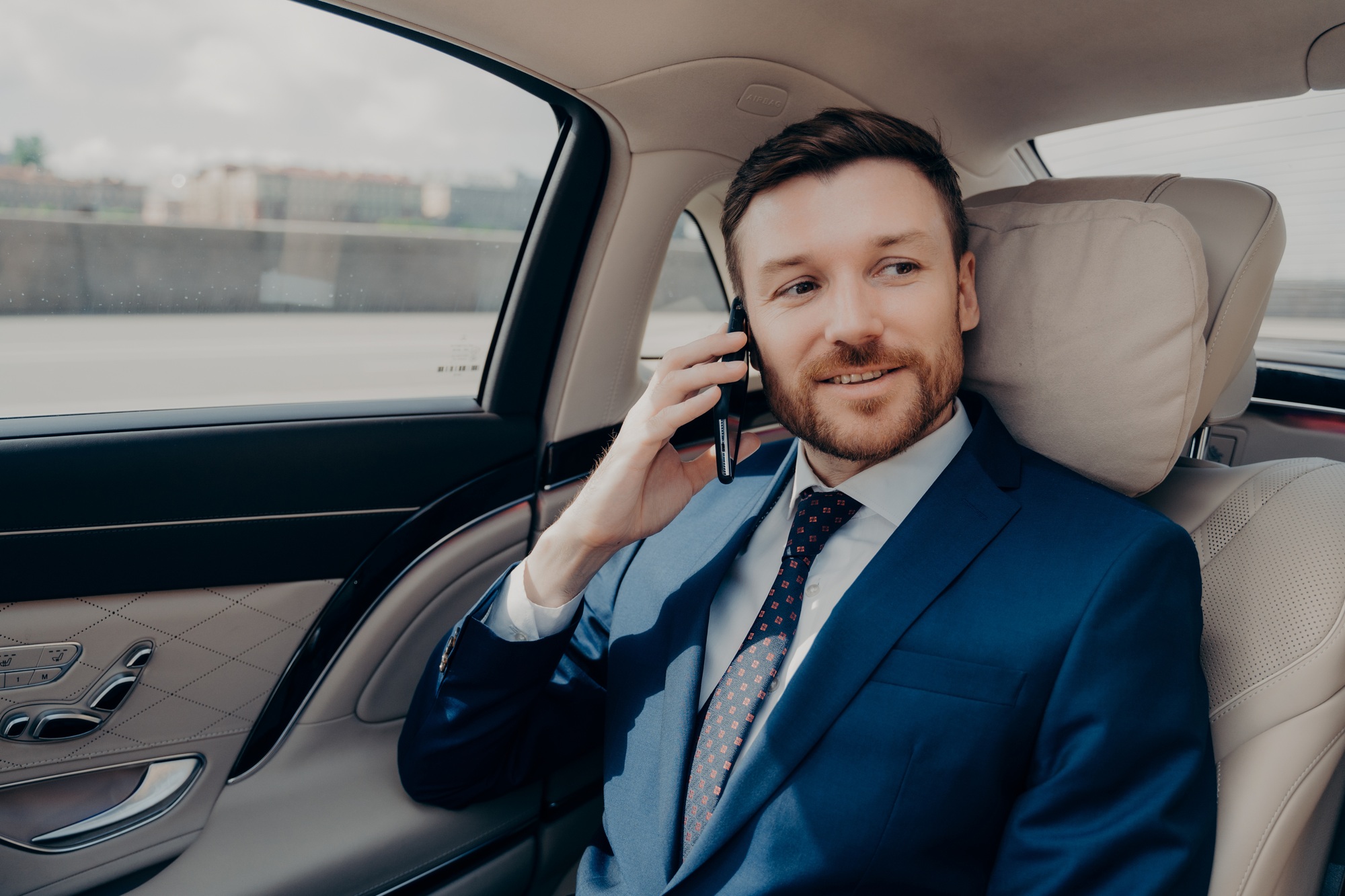 Young good looking businessman taking ride to conference while talking on phone